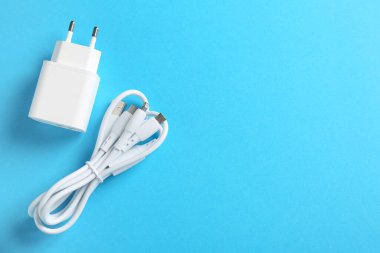 USB güç adaptörü ve açık mavi arka planda üçlü şarj kablosu, düz konum. Metin için boşluk