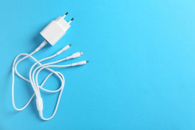 Açık mavi zemin üzerinde üçlü şarj kablosu olan USB güç adaptörü, üst görüş. Metin için boşluk