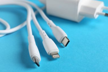 Açık mavi arkaplanda üç kat şarj kablosu ve USB güç adaptörü, yakın plan. Metin için boşluk