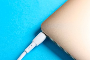 Açık mavi arkaplanda dizüstü bilgisayara bağlı USB şarj kablosu
