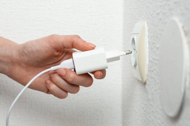 Kadın USB güç adaptörünü şarj kablosuyla kapalı mekandaki elektrik prizine takıyor.