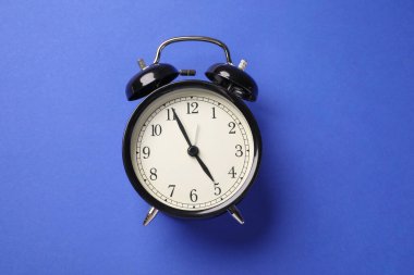 Mavi arkaplanda bir siyah alarm saati, üst görünümde.