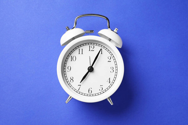 Один белый будильник на синем фоне, вид сверху