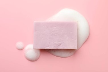 Açık pembe arka planda köpüklü sabun çubuğu, üst görünüm