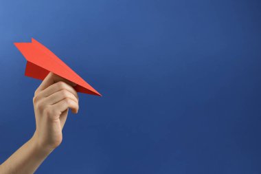 Mavi arka planda kırmızı kağıttan uçağı olan kadın, yakın plan. Metin için boşluk