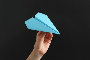 Siyah arka planda açık mavi kağıt uçağı olan kadın, yakın plan.