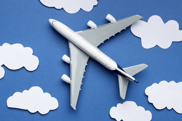 Plane model flying among paper clouds on blue background, flat lay