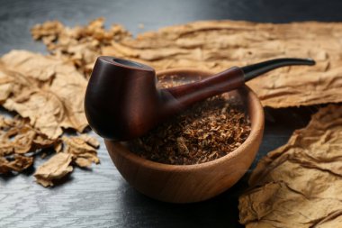 Tütün, kurumuş yapraklar ve siyah ahşap masada tüttürme piposu. Yakın plan.