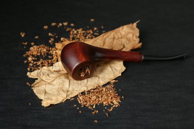Tütün, kurumuş yapraklar ve siyah ahşap masada tüttürme piposu. Yakın plan.