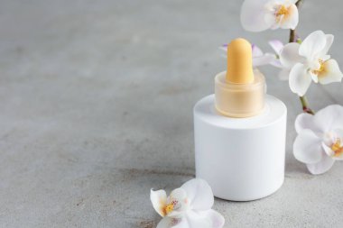 Gri desenli yüzeyde bir şişe cilt bakımı ürünü ve orkide çiçeği, metin için boşluk