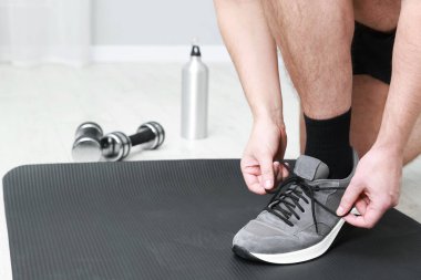 Ayakkabı bağcıklarını termik şişenin yanına bağlayan adam ve dambıllar içeride, yakın plan.