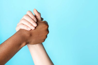 Irkçılığı bırak. Farklı ten renginde insanlar açık mavi arka planda el ele tutuşuyorlar, yakın plan. Metin için boşluk