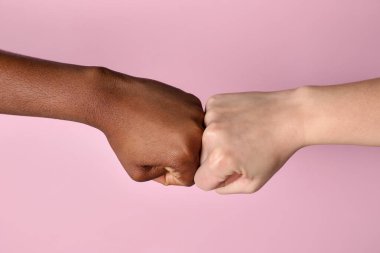 Irkçılığı bırak. Farklı ten renginde insanlar açık pembe arka planda yumruklaşıyorlar, yakın plan.