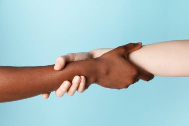 Irkçılığı bırak. Açık mavi arkaplanda el ele tutuşan farklı ten renginde insanlar, yakın plan