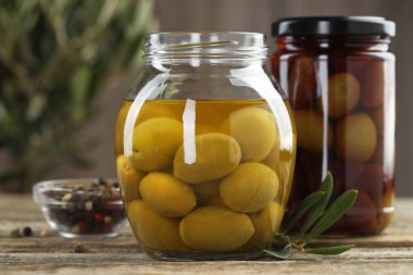 Cam kavanozlarda turşulu zeytin ve ahşap masada baharatlar, yakın plan.