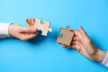 İş stratejisi ve takım çalışması konsepti. Ortaklar bulmaca parçalarını açık mavi arkaplanda birleştiriyor, yakın plan