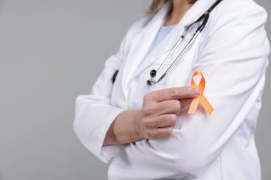 Çoklu Skleroz farkındalığı. Açık gri arka planda turuncu kurdeleli doktor, yakın plan.