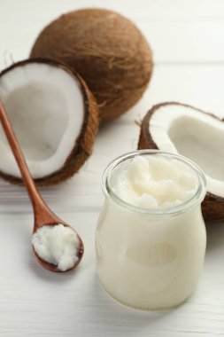 Cam kavanozda organik hindistan cevizi pişirme yağı, kaşık ve beyaz ahşap masada taze meyveler, yakın plan.