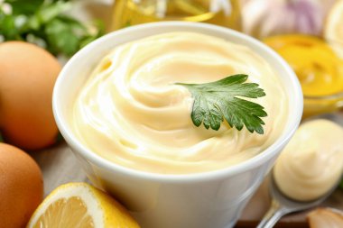 Lezzetli mayonez sosu kasede ve malzemeler masada, yakın plan.