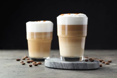Bardakta latte macchiato ve gri masada kahve çekirdekleri, yakın plan.