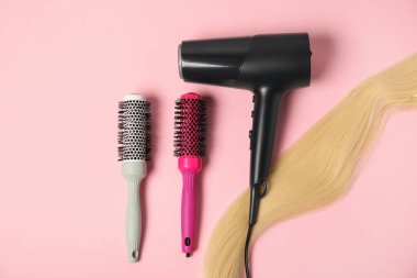 Havalı yuvarlak fırçalar, bir tutam sarı saç ve pembe arka planda saç kurutma makinesi, düz yatış.
