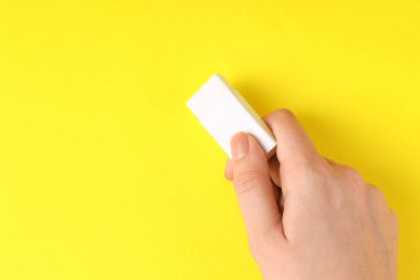 Sarı arka planda silgi kullanan bir kadın, yakın plan. Metin için boşluk