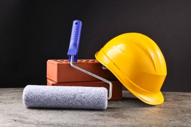 Tuğla, şapka ve boya silindiri gri masada.