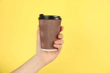 Sarı arka planda kağıt bardak tutan kadın, yakın plan. Tasarım için model