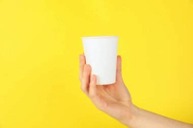 Sarı arka planda kağıt bardak tutan kadın, yakın plan. Tasarım için model