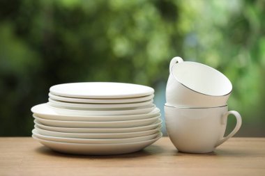 Temiz bulaşık takımları ve bardaklar ahşap masada bulanık yeşil arka plana karşı