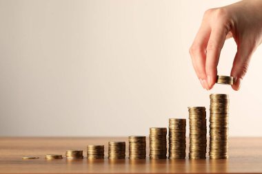 Ahşap masadaki para yığınlarına para koyan kadın gri arka planda, yakın plan. Metin için boşluk