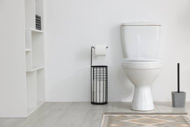 Tuvalet, fırça ve ihtiyaçlar banyoda beyaz duvarın yanında.