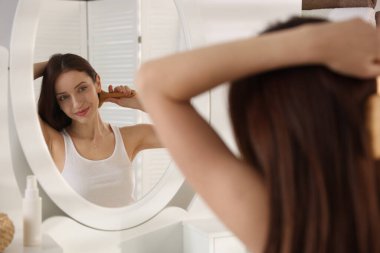 Güzel bir kadın saçını aynanın yanında tarıyor, seçici bir odak noktası var.