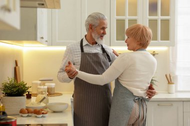 Mutfakta yemek yaparken dans eden yaşlı çift.