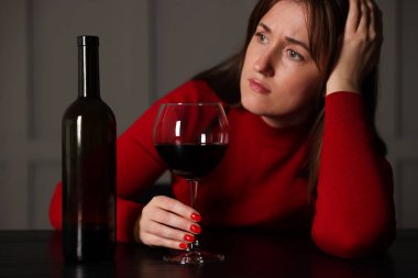 Alkol bağımlılığı. İçerideki ahşap masada kırmızı şarap ve şişe taşıyan kadın.