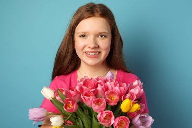 Açık mavi arka planda bir buket lalesi olan güzel genç kız.