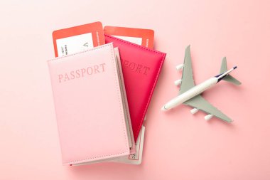 Biletli pasaportlar ve pembe arka planda uçak modeli, düz konum