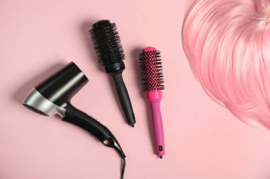 Havalı yuvarlak fırçalar, saç kurutma makinesi ve pembe arka planda bir tutam boyalı saç, düz yatış.