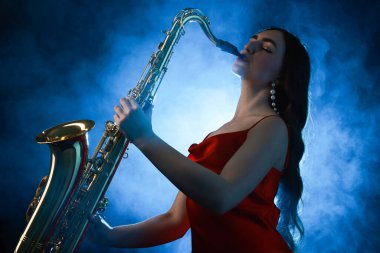 Profesyonel müzisyen koyu arkaplanda mavi ışık ve dumanla saksafon çalıyor.