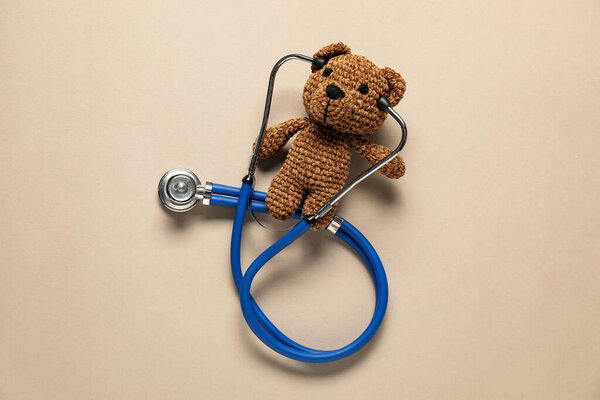 Pediatrics concept. Toy bear with stethoscope on beige background, top view