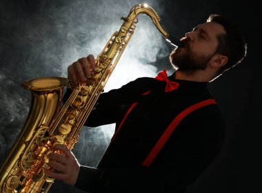Profesyonel müzisyen siyah arkaplanda dumanla saksafon çalıyor.