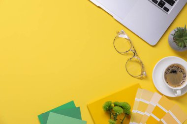 Dizüstü bilgisayarı, kırtasiyesi ve sarı arka planda bir fincan kahvesi olan tasarımcı işyeri. Metin için boşluk