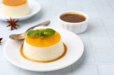 Tasty pudding with caramel sauce served on white tiled table, closeup. Space for text