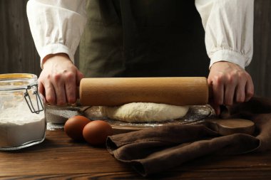 Ahşap masada merdaneyle hamuru şekillendiren kadın, yakın plan.