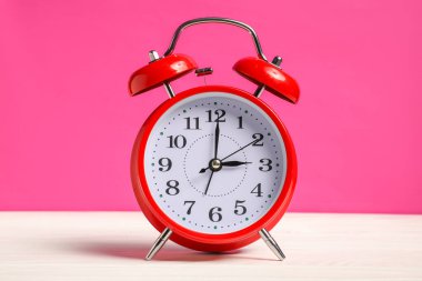 Beyaz ahşap masada parlak pembe arka planda kırmızı bir çalar saat.