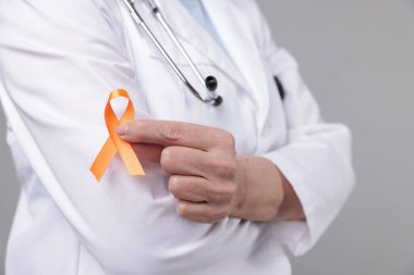 Çoklu Skleroz farkındalığı. Açık gri arka planda turuncu kurdeleli doktor, yakın plan.