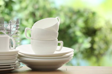 Farklı temiz bulaşık takımları, fincanlar ve çatal bıçak takımı. Bulanık yeşil arkaplan, metin için boşluk.