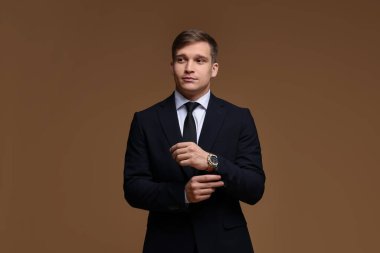 Kahverengi arka planda şık saati olan klasik takım elbiseli bir adam.