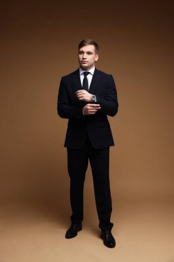 Kahverengi arka planda şık saati olan klasik takım elbiseli bir adam.