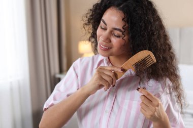 Gülümseyen genç kadın evde tarağıyla kıvırcık saçlarını tarıyor.
